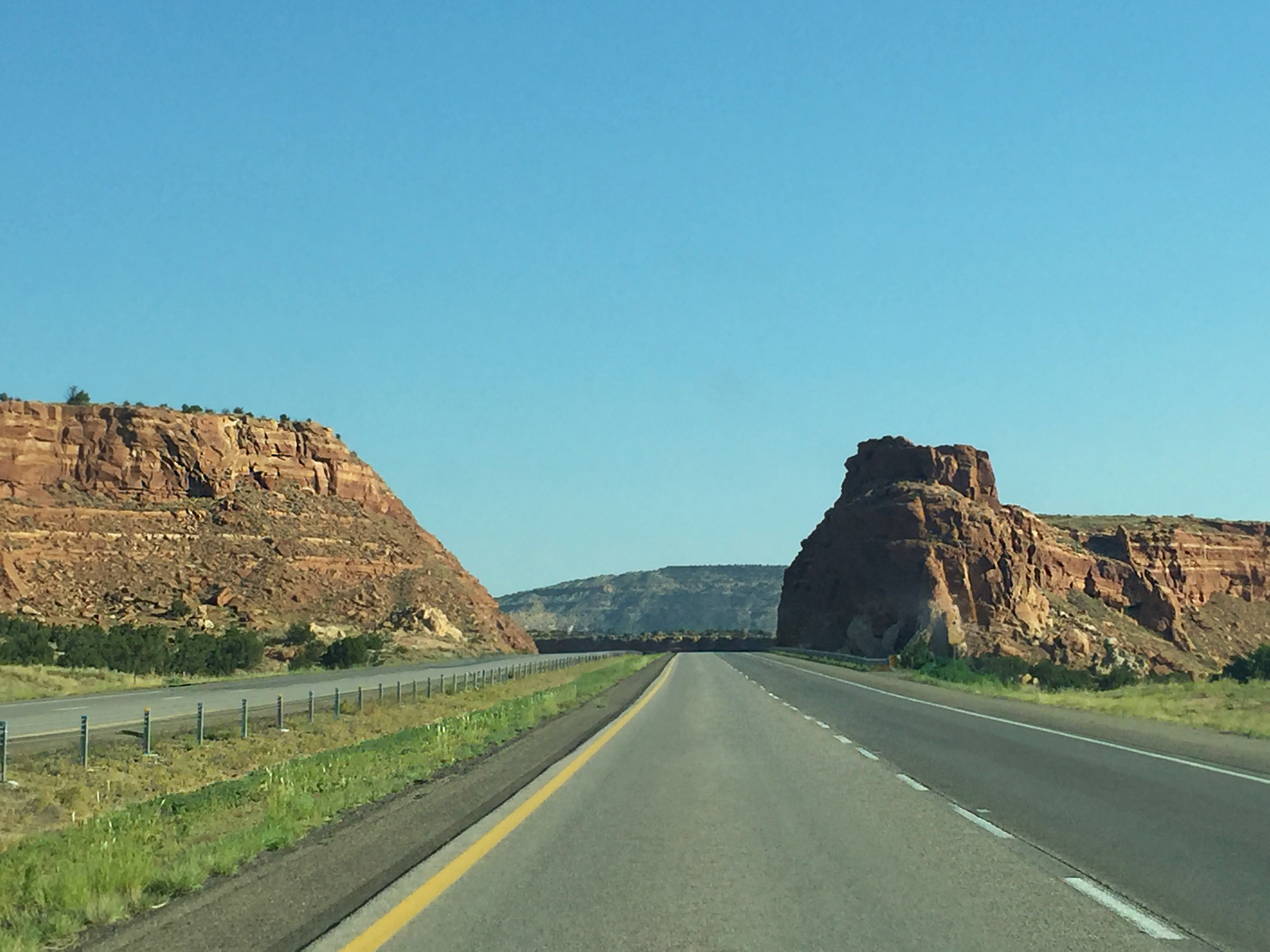 Straight desert highway cutting between red rock mesas under a clear blue sky